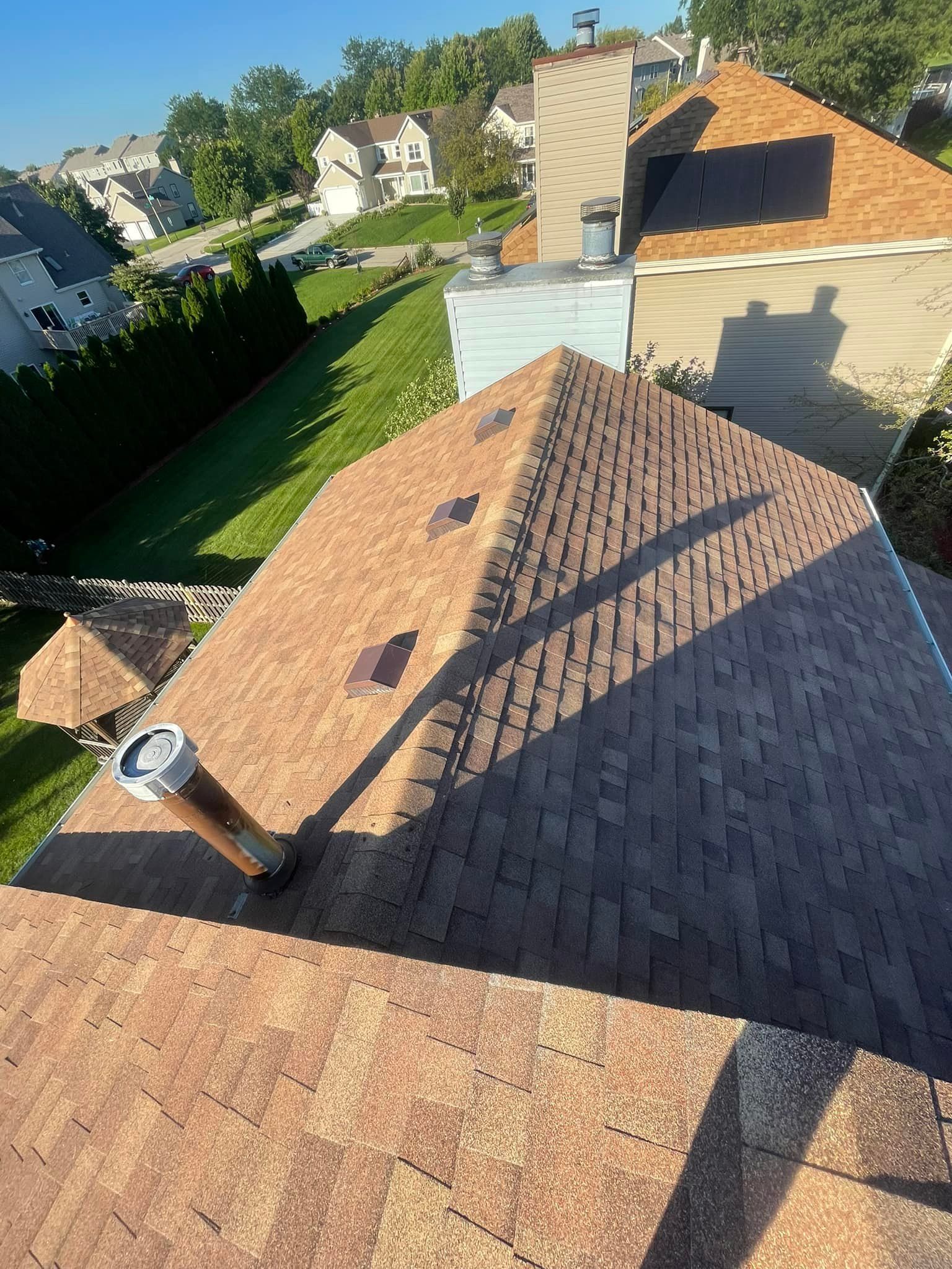 Brown shingle roof with vents. The roof is on a house surrounded by green grass and trees.