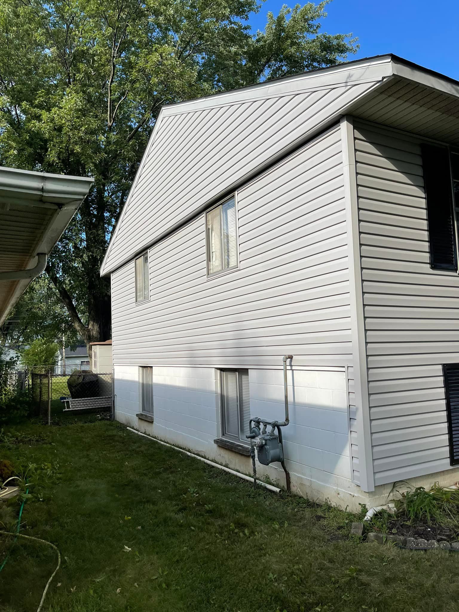 Two-story house with gray siding, windows, and green lawn.