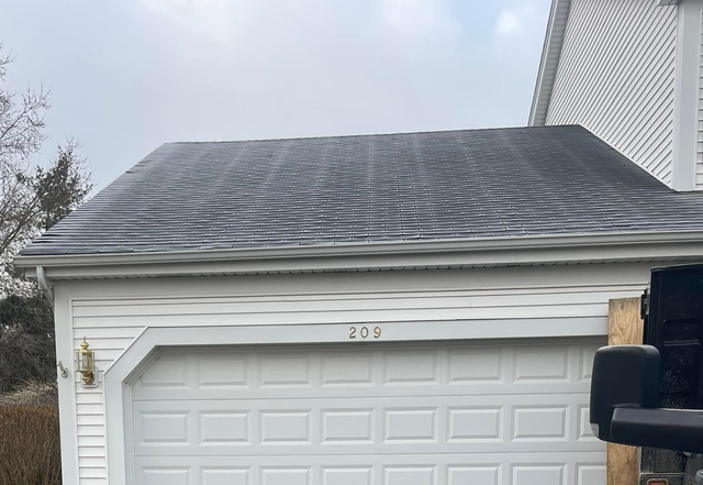Garage with white door and gray roof. The roof has a pattern. The garage has the number 205. Cloudy sky.