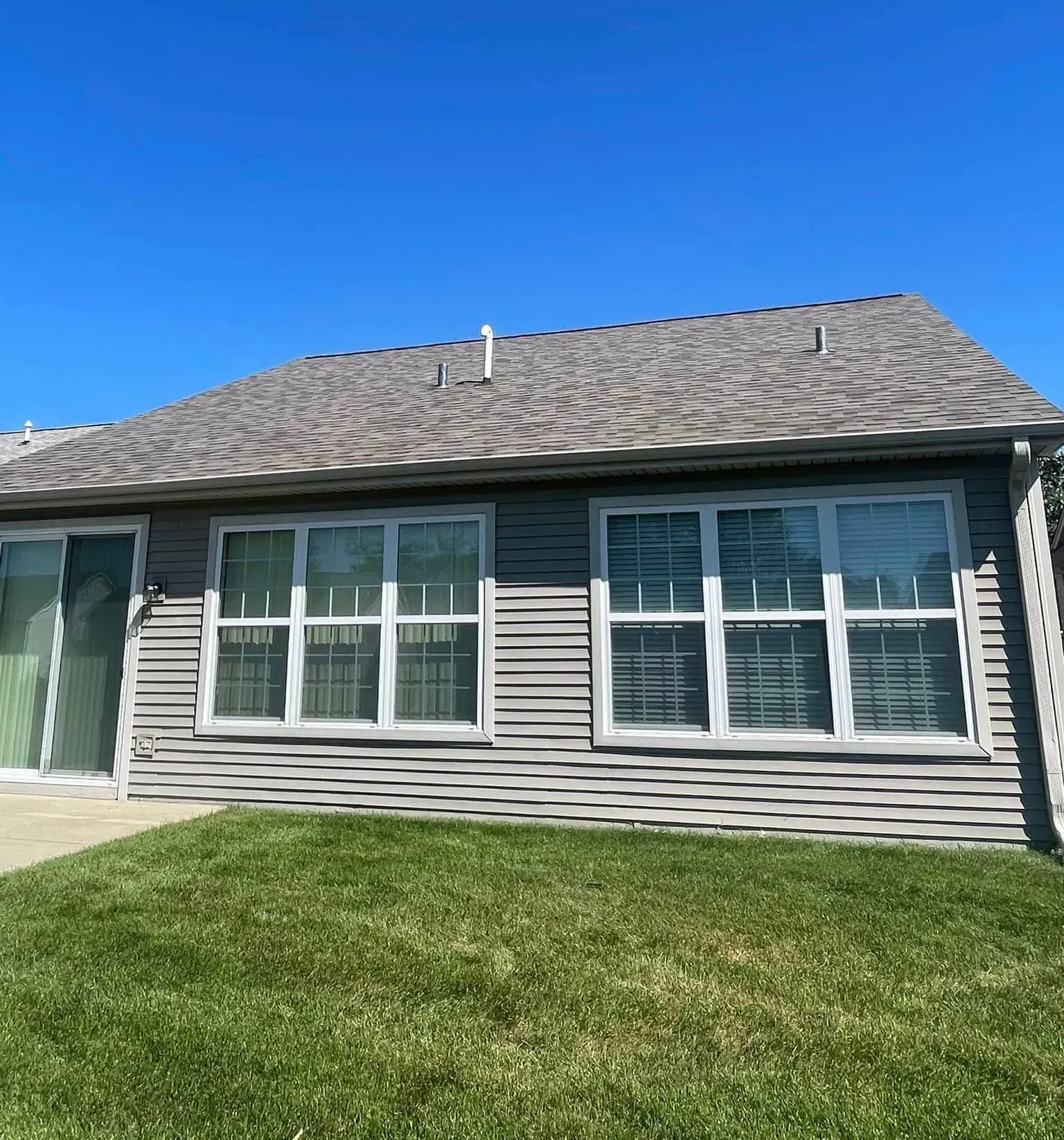 Gray house with windows and a sloping roof, set against a clear blue sky and green grass.