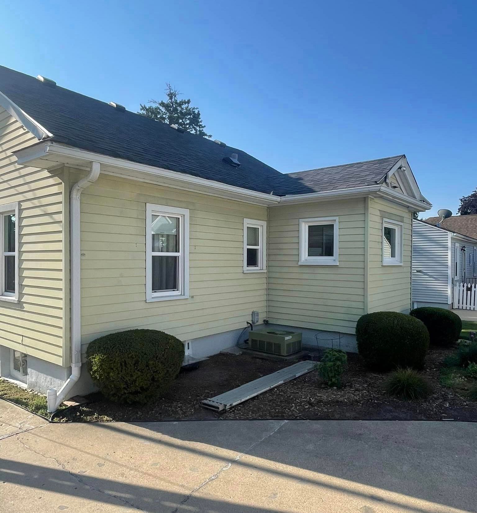 Yellow house with white trim and bushes, on a sunny day.