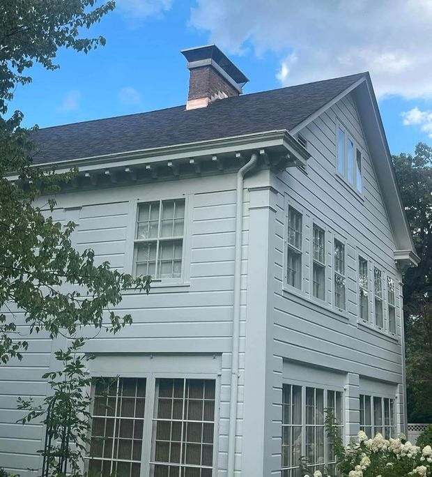 White house with dark roof and brick chimney against a blue sky.
