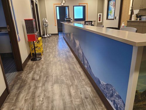 Dental office reception desk with a mountain graphic. Wooden floors, a gumball machine, and doors.