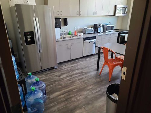 A modern office kitchen with stainless steel appliances, cabinets, and a table with an orange chair.