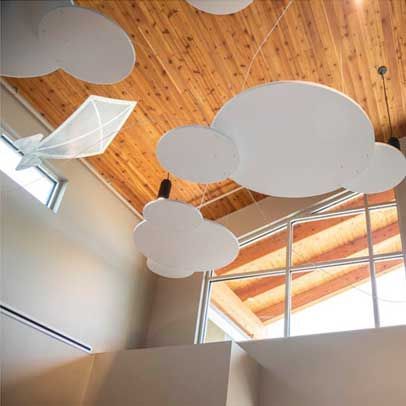 Cloud-shaped decorations hang from a wooden ceiling in a building with large windows.