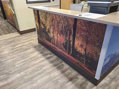 Reception desk with autumn forest scene and gray wood-look floor.