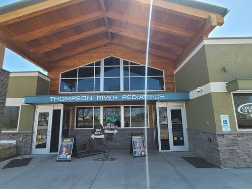 Thompson River Pediatrics entrance: tan wood and green building with sign, glass windows, and entrance doors.