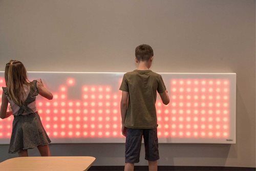 Two children interact with a large, glowing red interactive wall display.