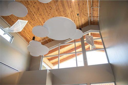Clouds and kites suspended from a wood-paneled ceiling above a large window.