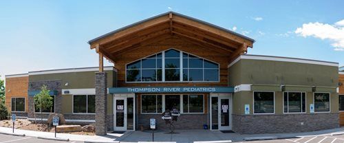 Exterior of Thompson River Pediatrics building, with a wooden roof, and a blue sky.