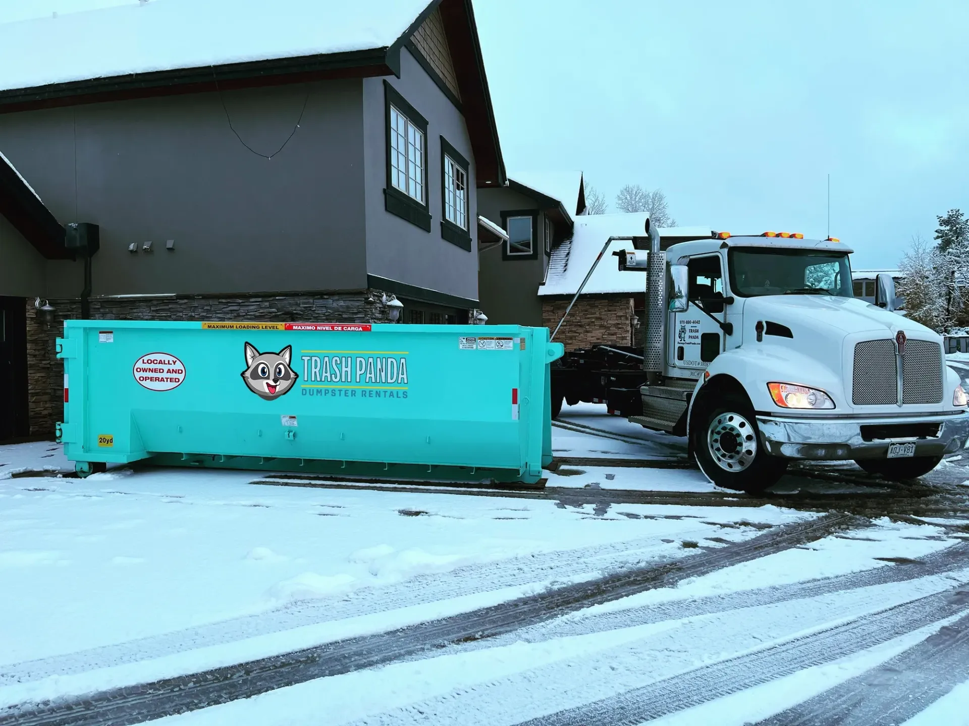 A dumpster is parked in front of a house in the snow.