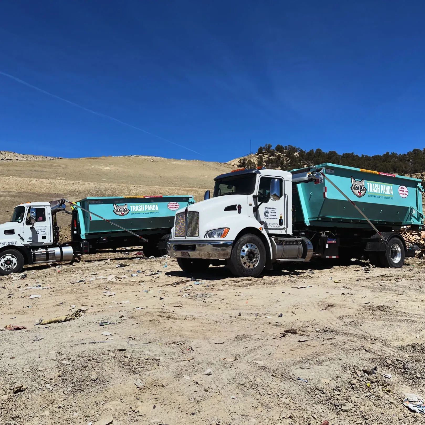 Two dump trucks are parked next to each other in a dirt field