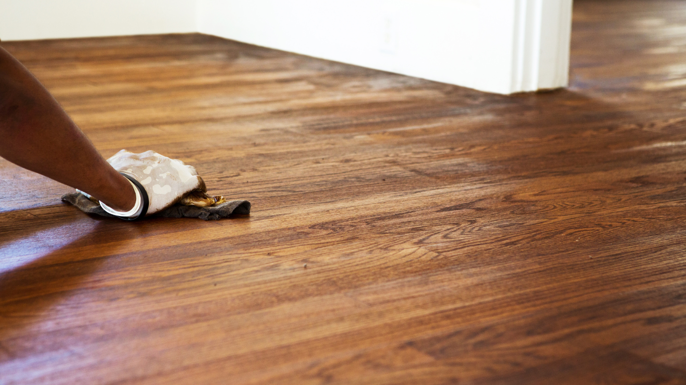 A person is cleaning a wooden floor with a cloth.