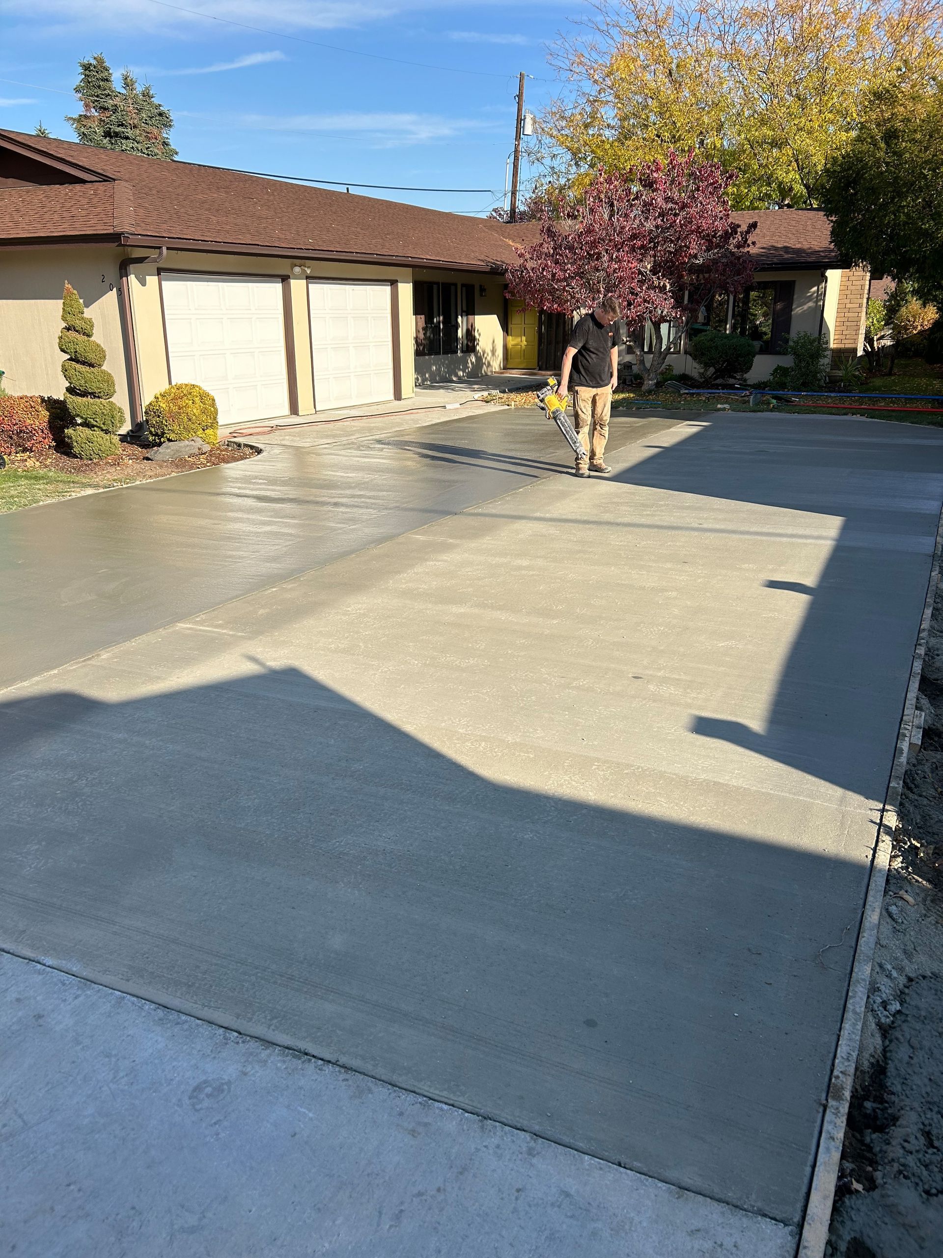 A man is walking down a concrete driveway in front of a house.