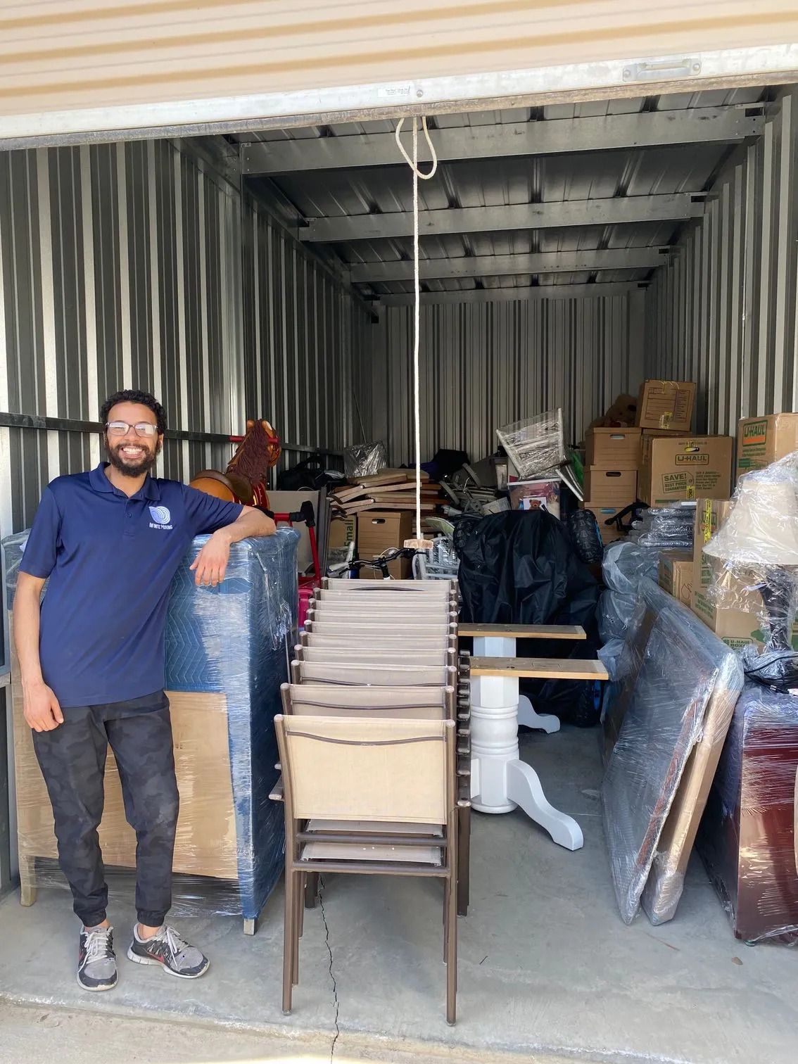 Man standing in a storage container filled with furniture and boxes.