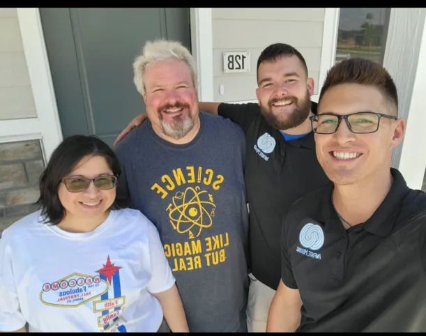 Four people smiling in front of a house. Two men wear staff shirts, the other two wear casual clothing.
