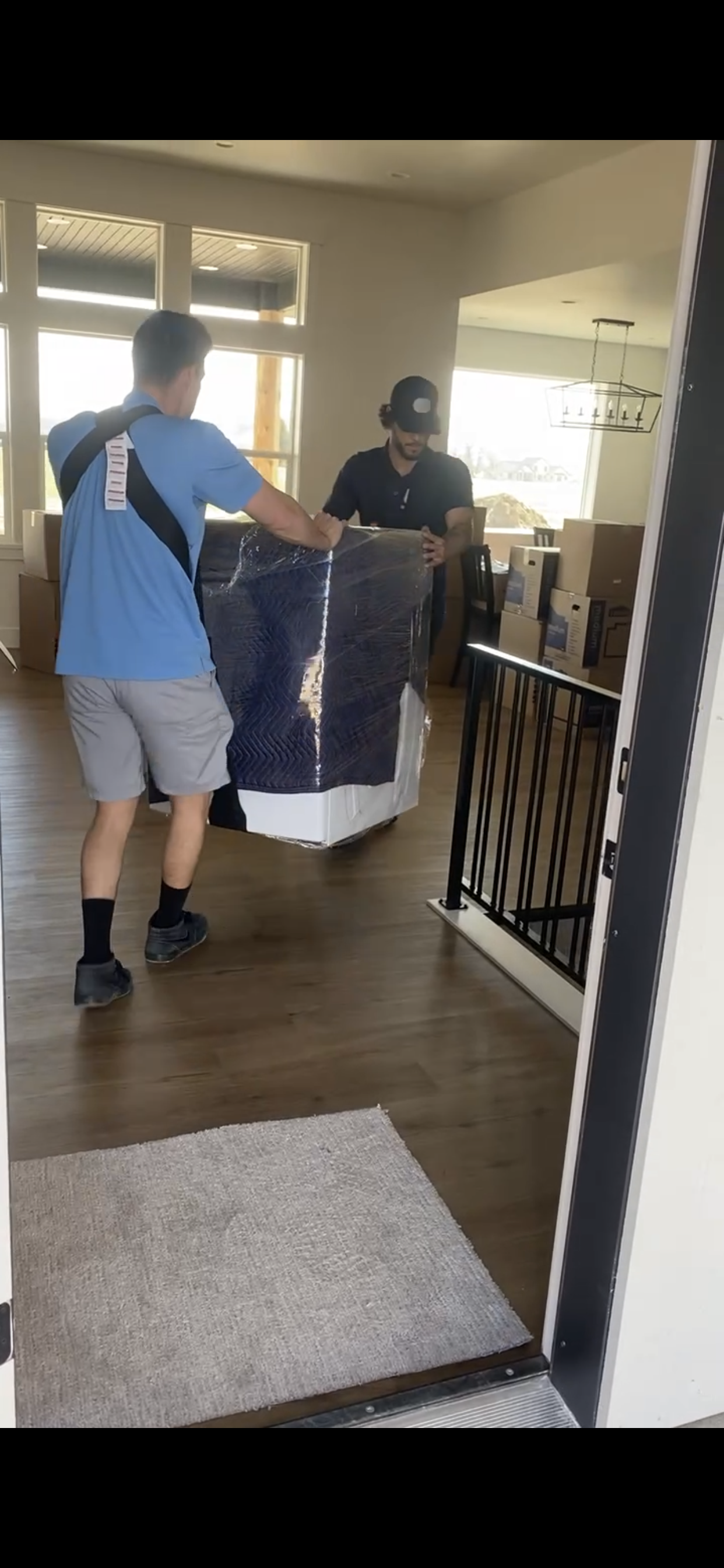 Two men are carrying a refrigerator in a living room.