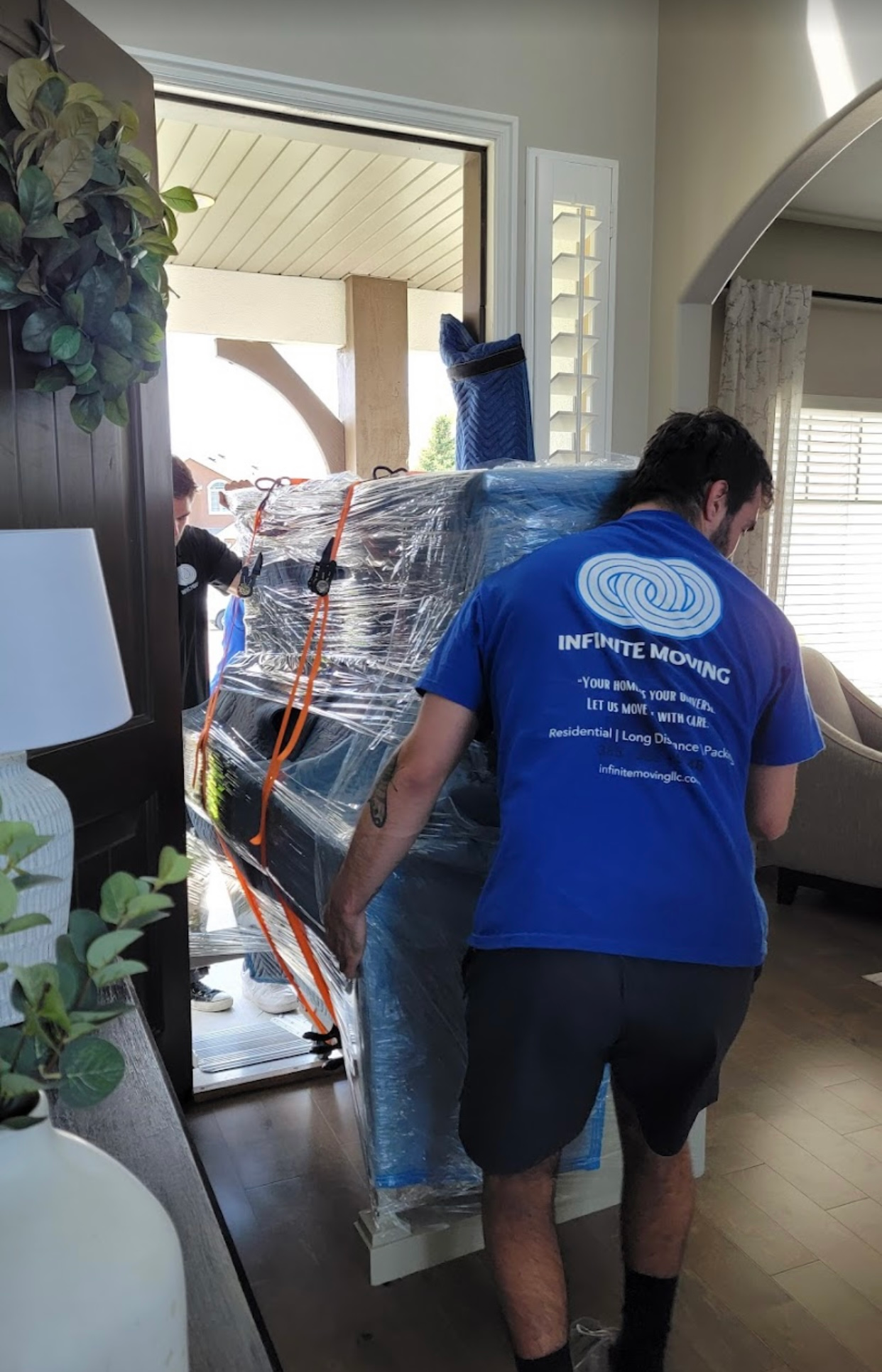 A man in a blue shirt is carrying a piano in a living room.