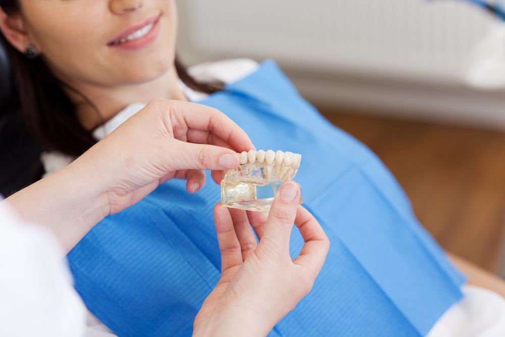 A Woman Is Sitting In A Dental Chair While A Dentist Holds A Model Of Her Teeth — Mittagong Dental Care In Mittagong, NSW
