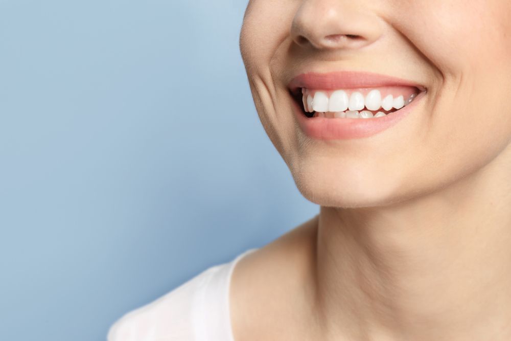 Woman smiling, showing white teeth, against a blue background.