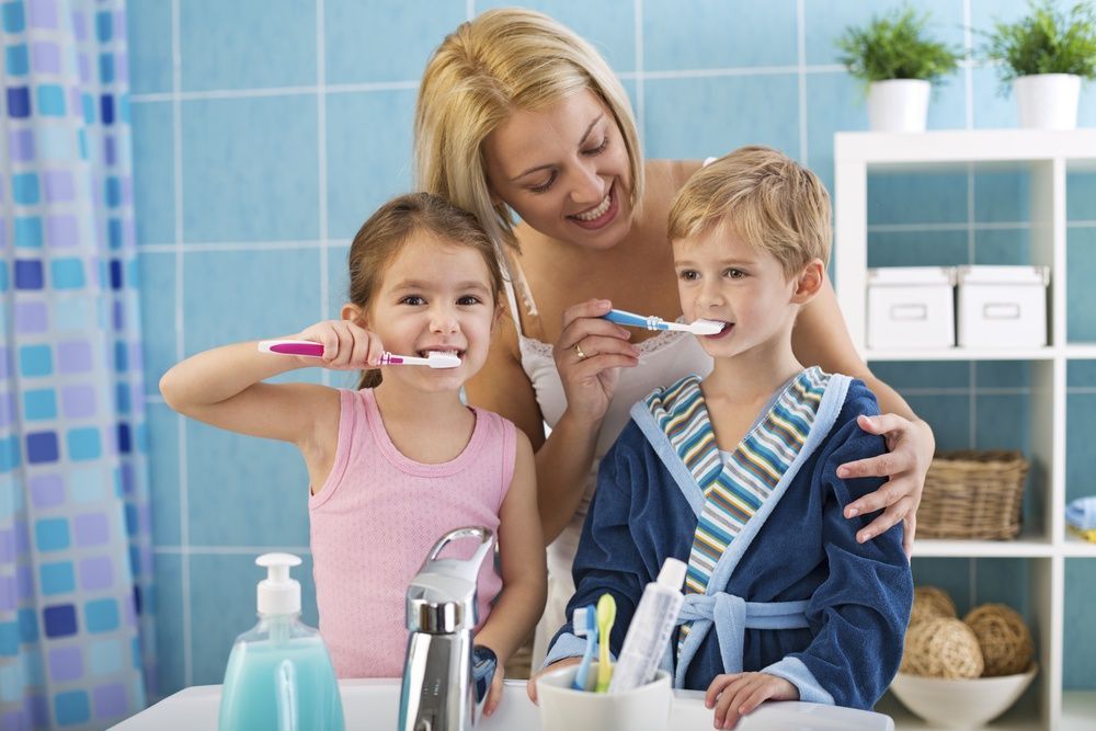 A Woman and Two Children Are Brushing Their Teeth — Mittagong Dental Care In Mittagong, NSW