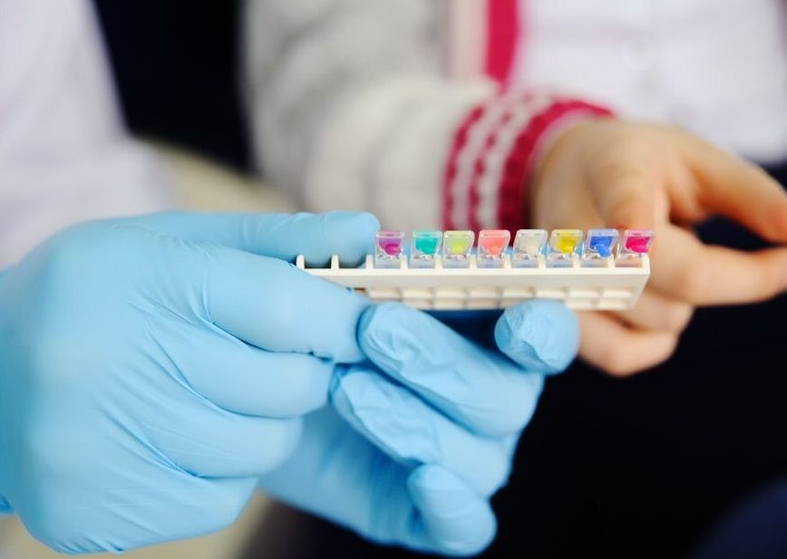 A Person Wearing Blue Gloves Is Holding A Tray Of Test Tubes — Mittagong Dental Care In Mittagong, NSW