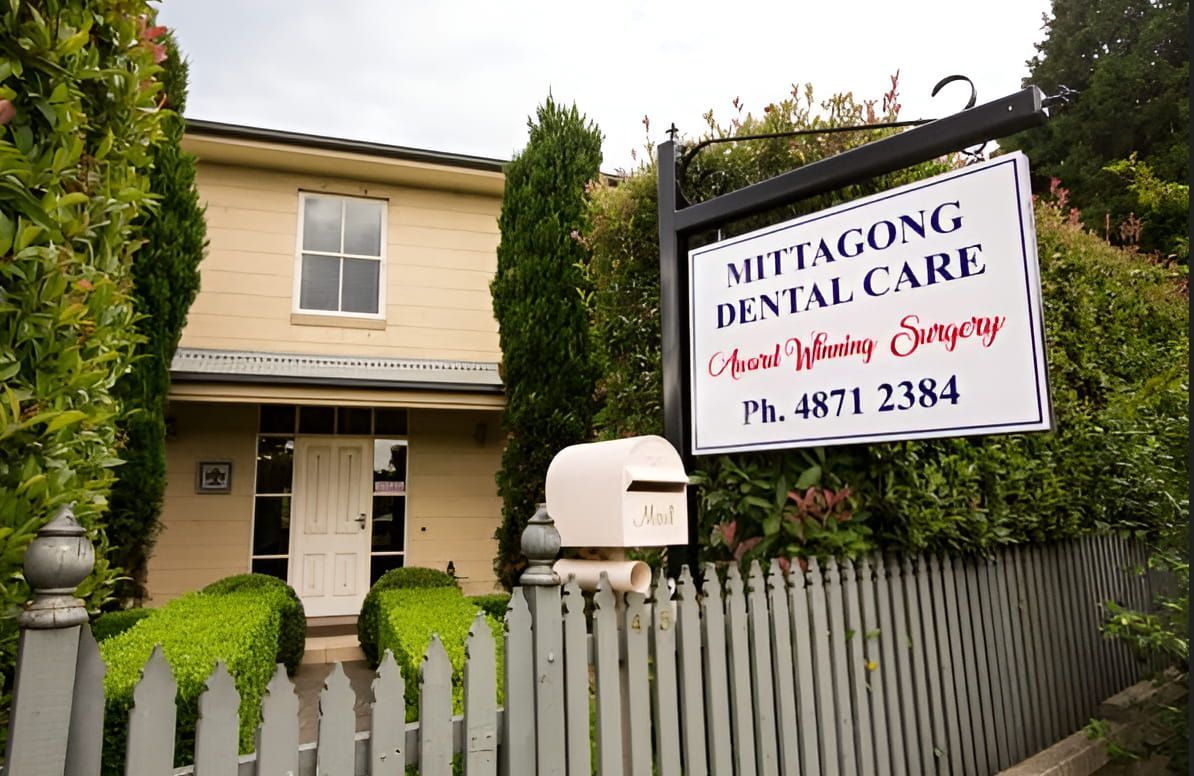 A Sign For Mittagong Dental Care Hangs Over A Fence — Mittagong Dental Care In Mittagong, NSW