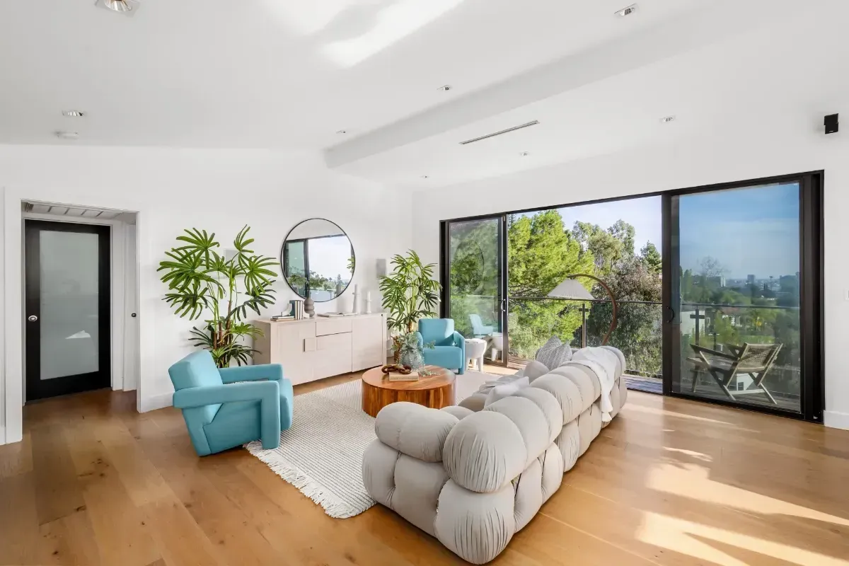 Bright modern living room with teal chairs, white sofa, wood floors, and large windows opening to a city view - Calimesa CA Kearney Restorations