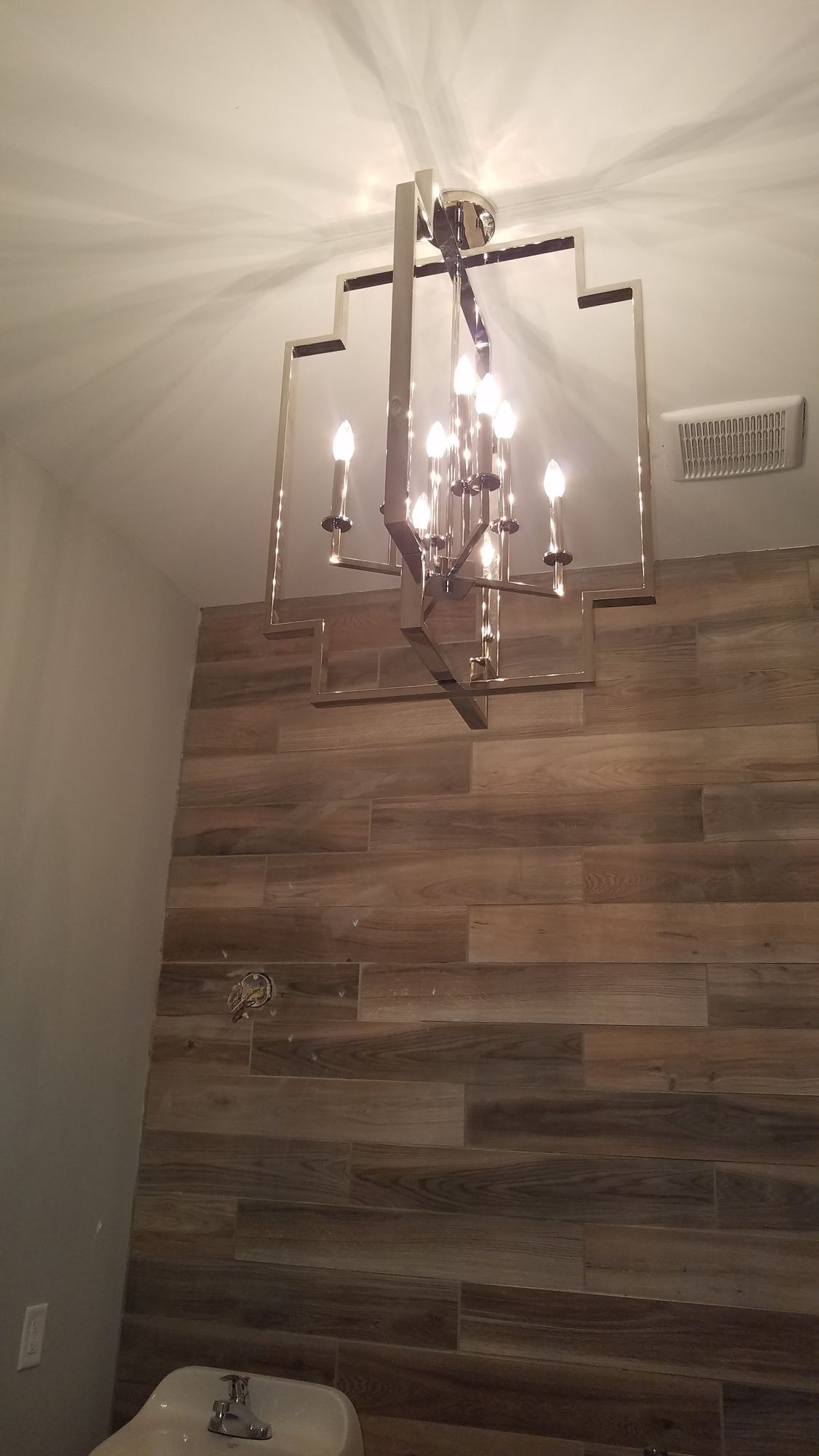 A bathroom with a wooden wall and a chandelier hanging from the ceiling.