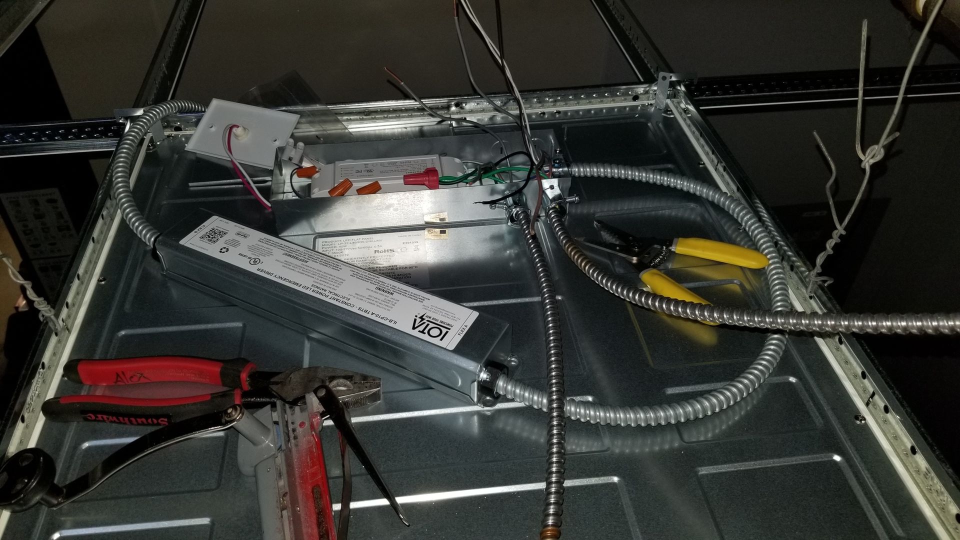 A ceiling light is being installed with tools and wires.