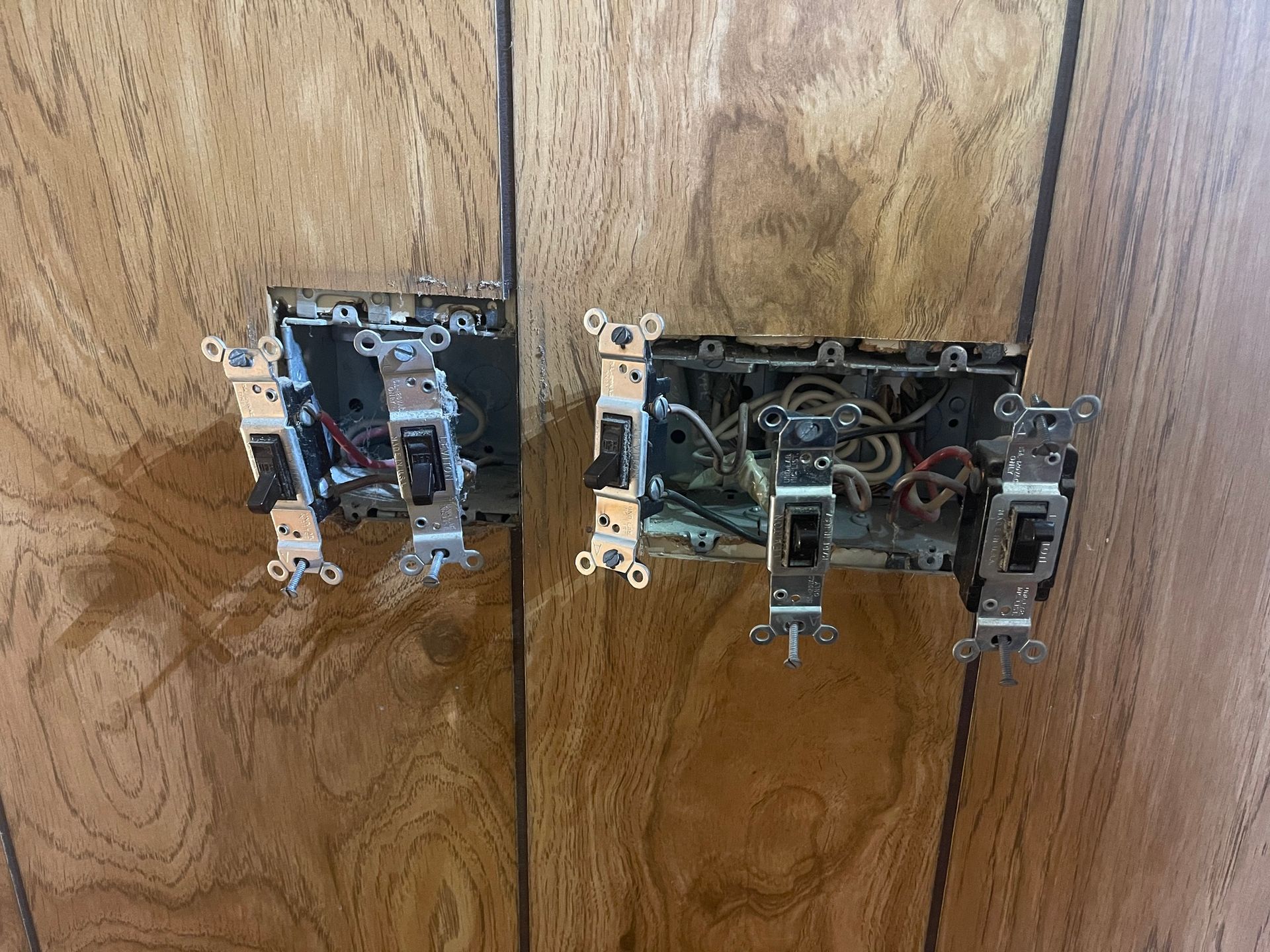 Two light switches are sitting on a wooden wall.