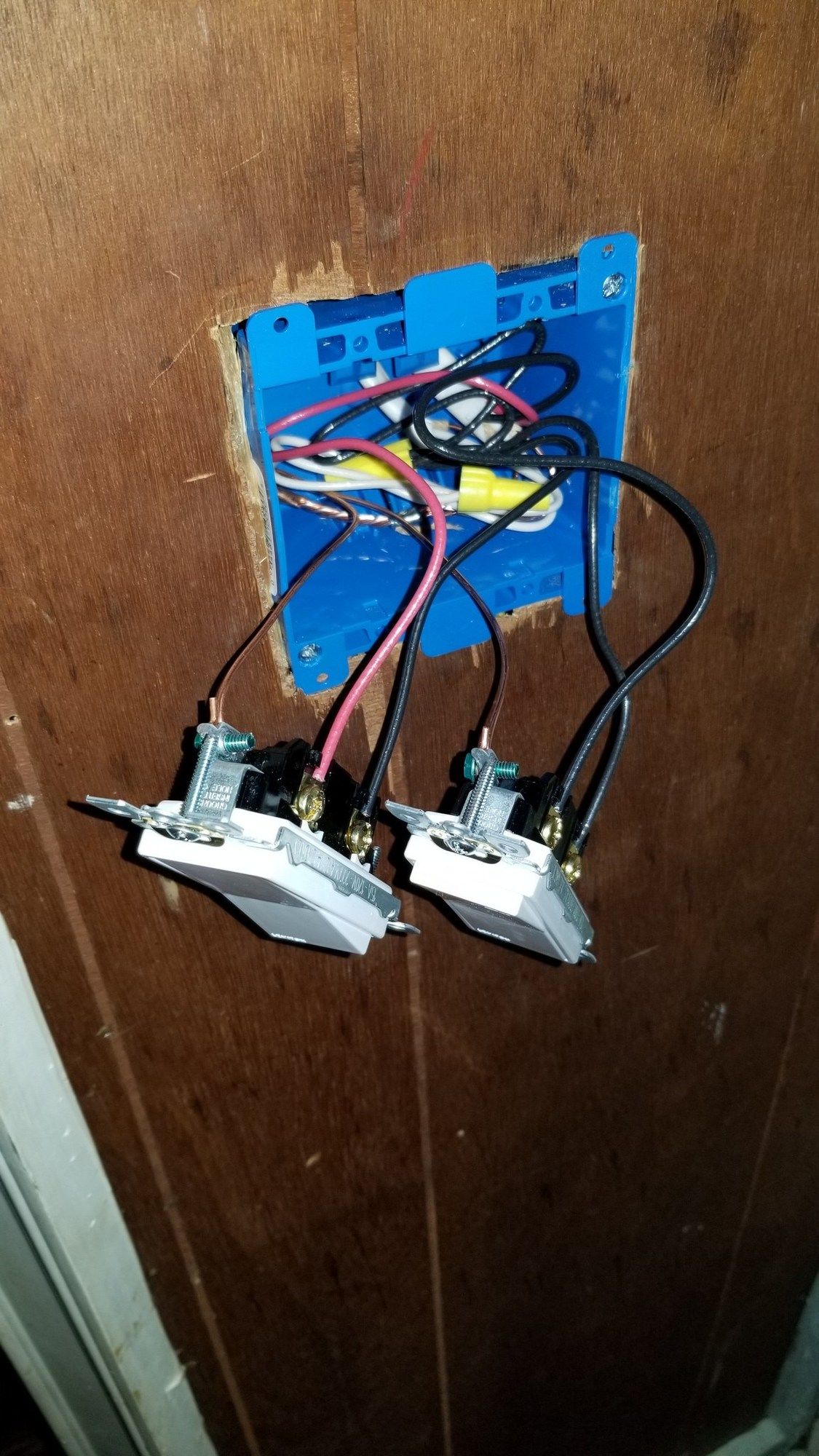 Two light switches are being installed on a wooden wall.