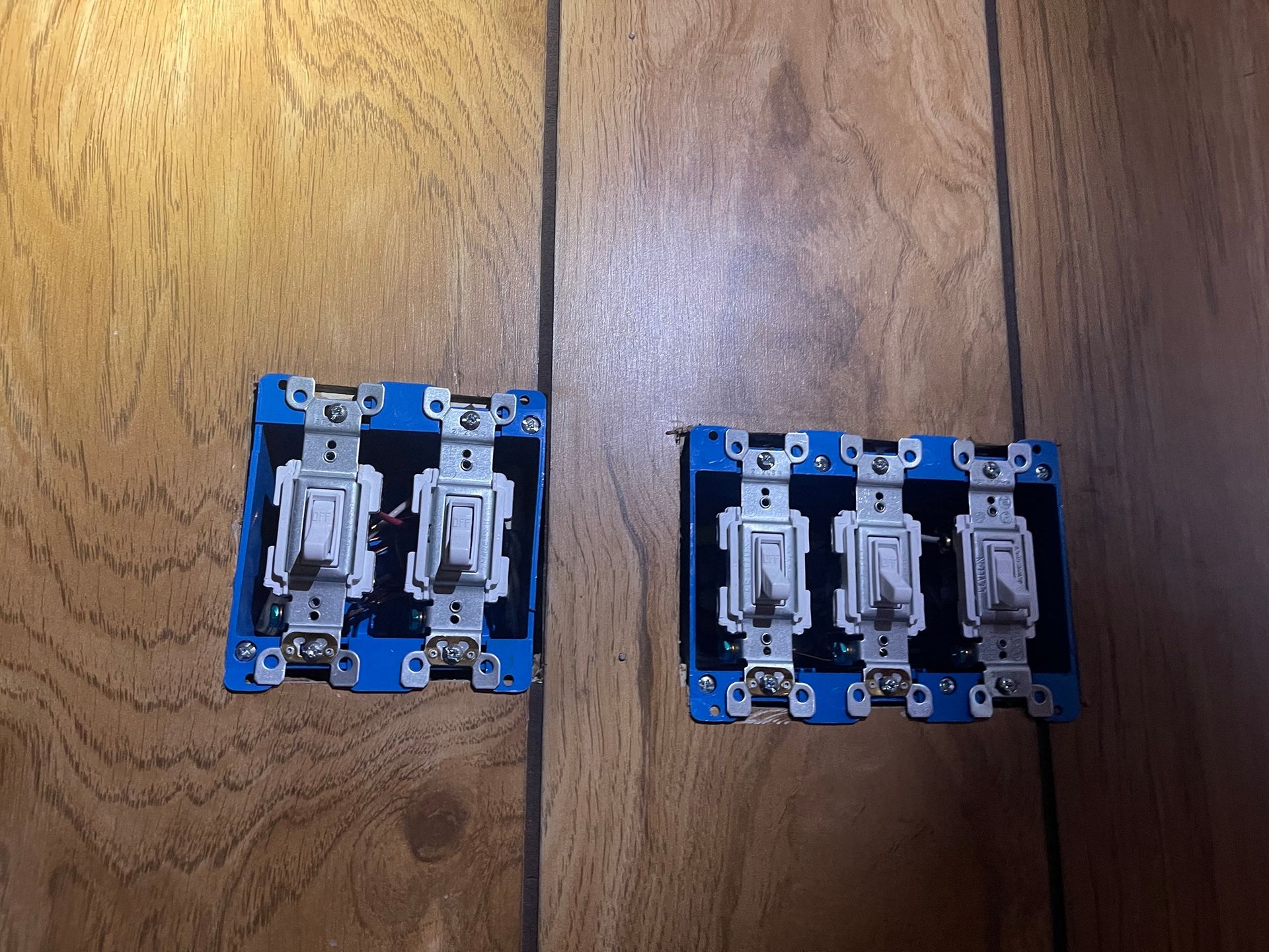 Two light switches are sitting on a wooden floor.