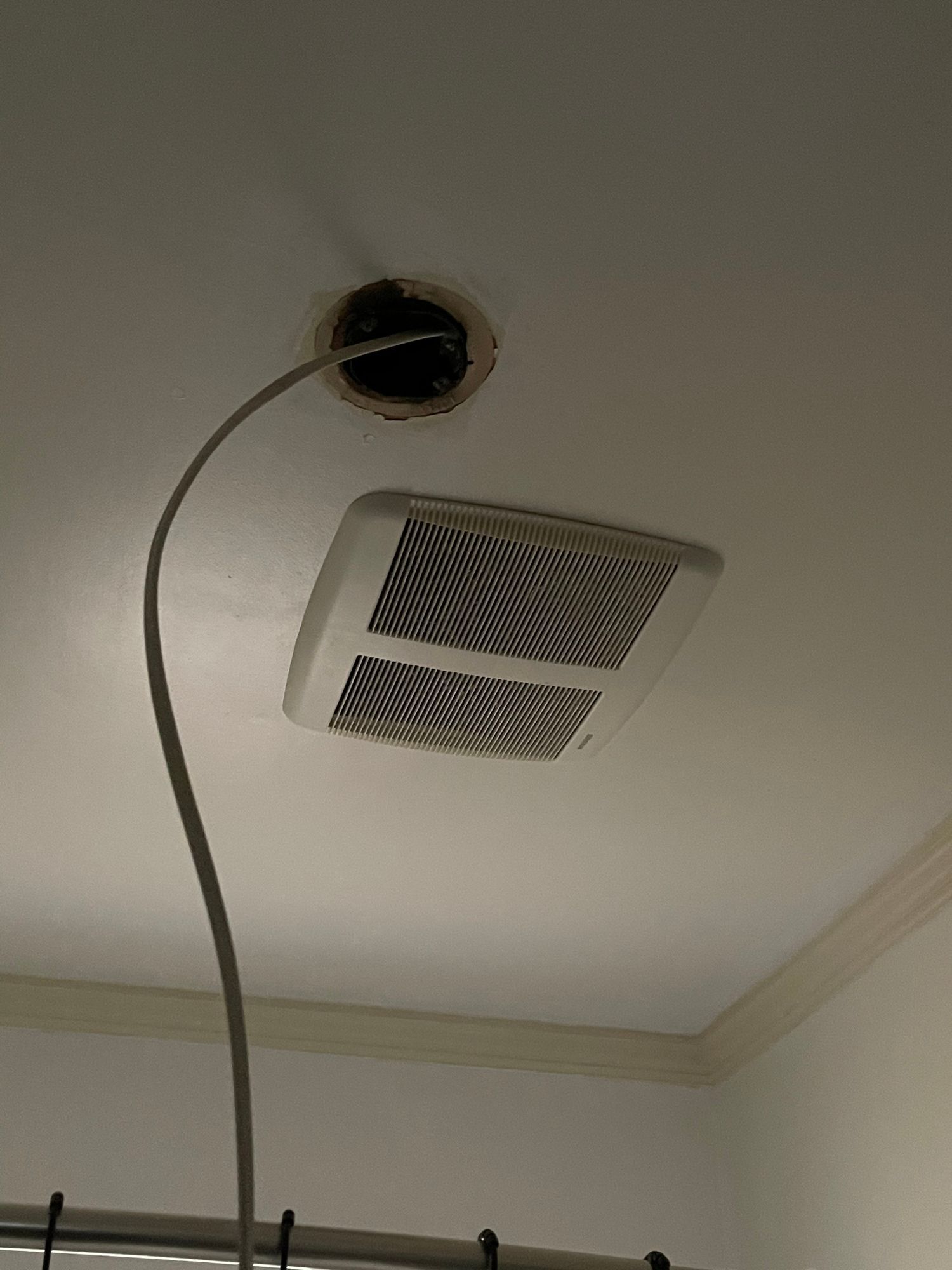 A fan is hanging from the ceiling of a bathroom next to a shower curtain.