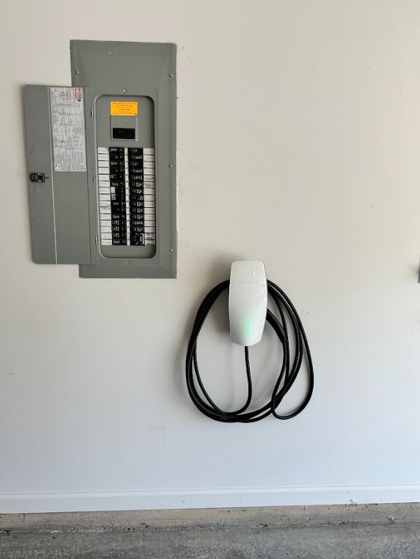A tesla charging station is attached to a wall in a garage.