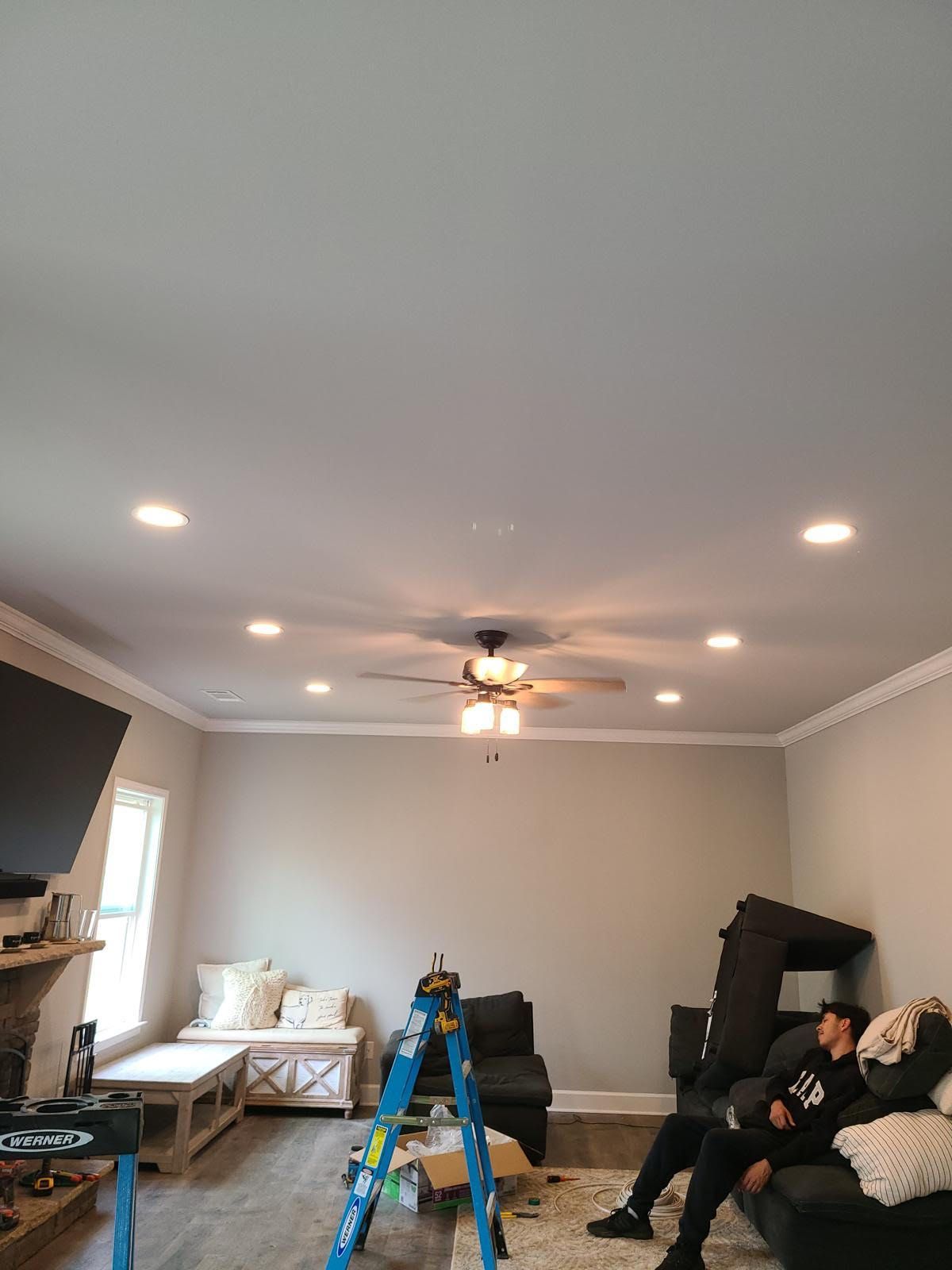 A man is sitting on a couch in a living room with a ceiling fan.