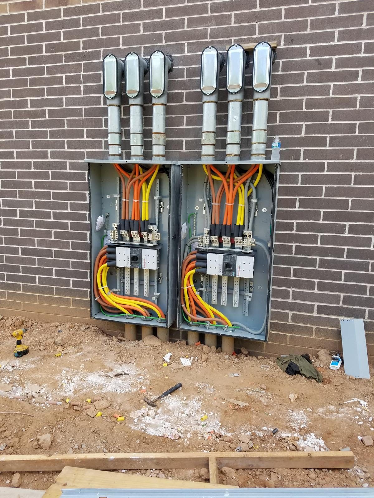 Two electrical boxes are sitting on the ground in front of a brick wall.
