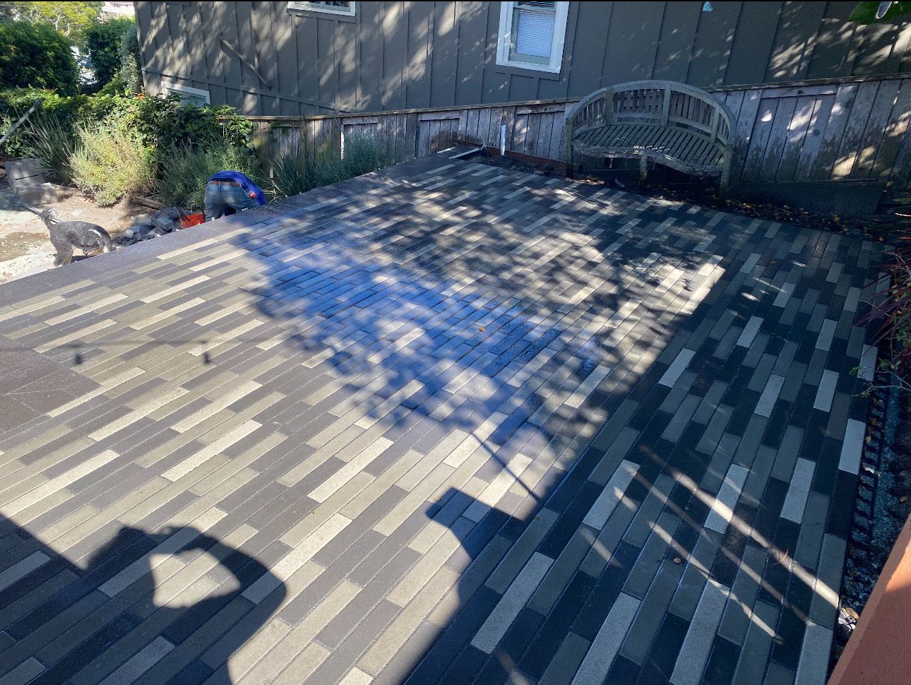 A person's shadow on a rooftop, with various shades of gray shingles. Sunlight, outdoor setting.