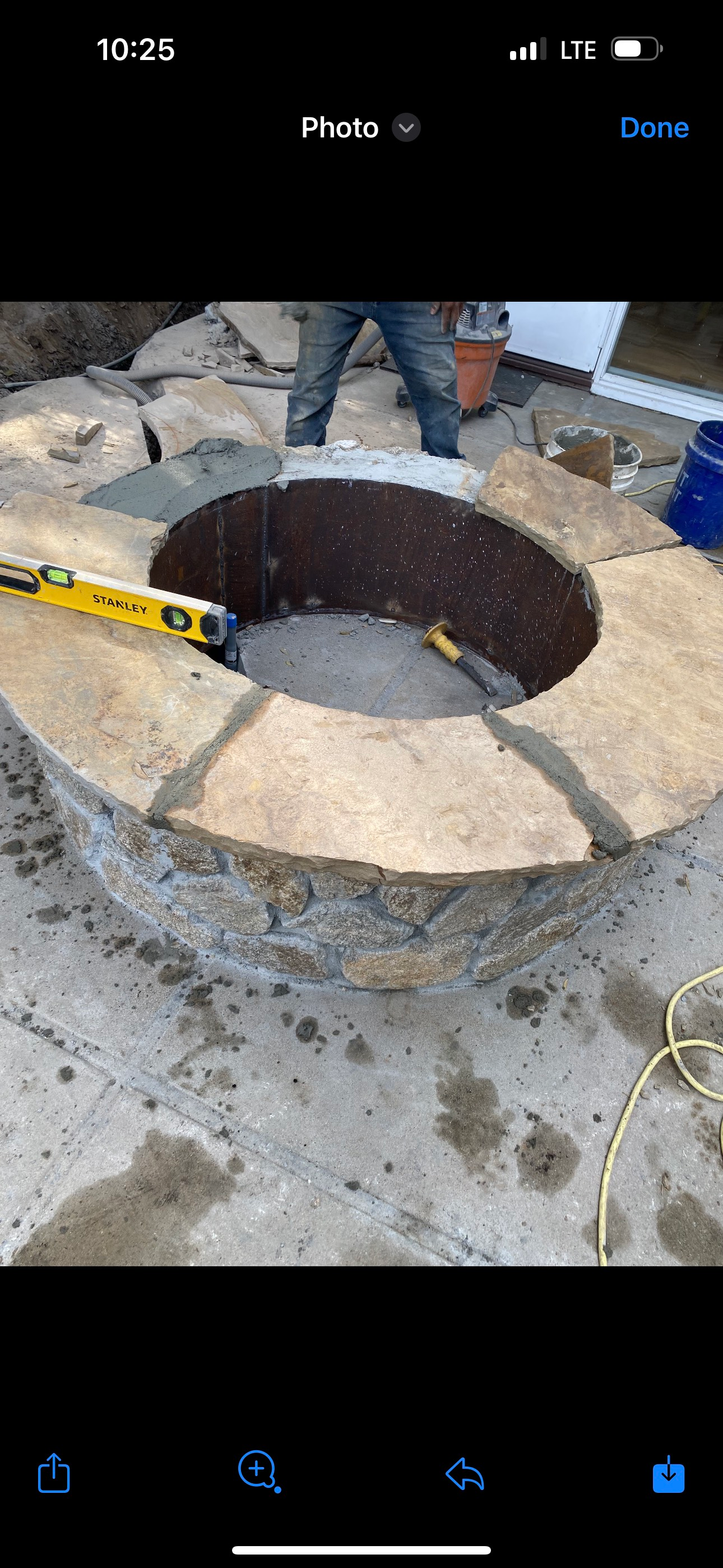 Construction of a fire pit with a circular stone surround and central opening. A person is standing nearby.