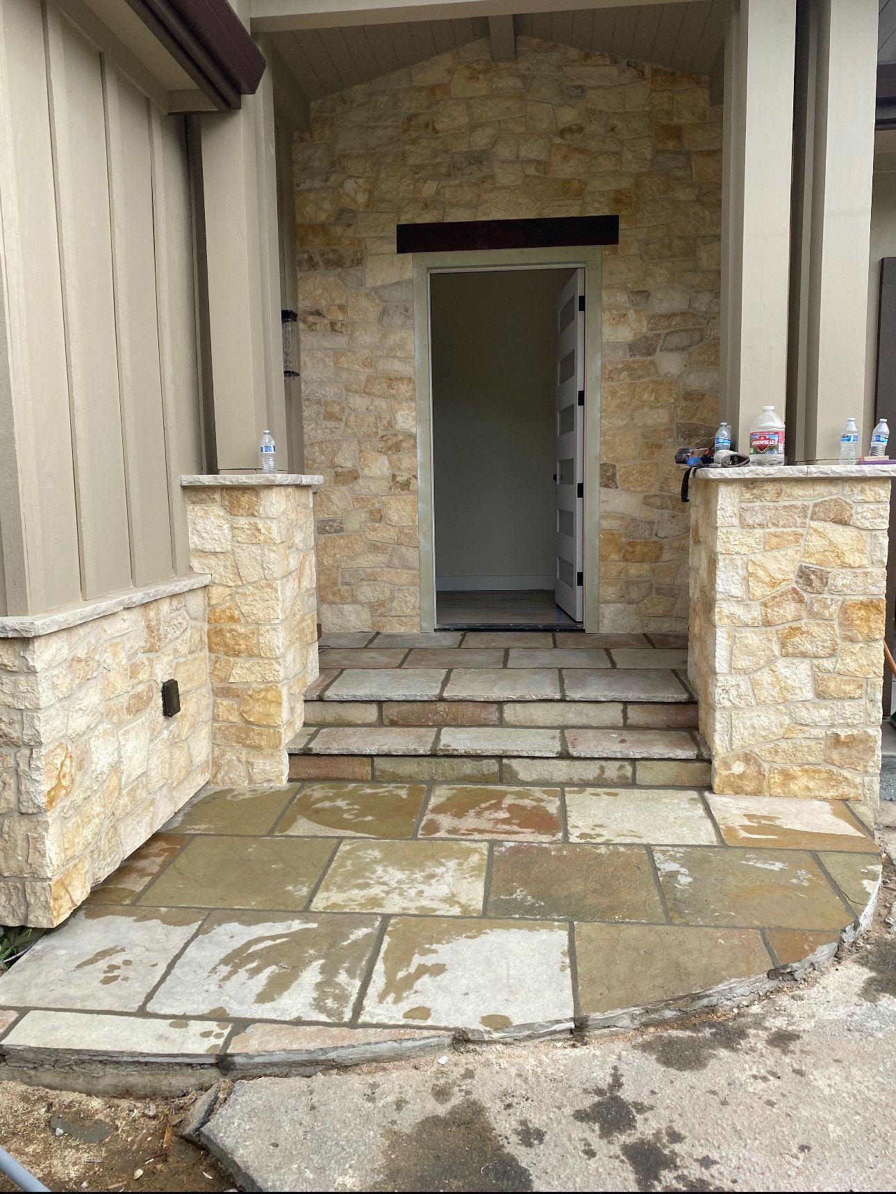 Entrance with stone steps, pillars, and wall. Doorway framed in stone. Wet stone path.