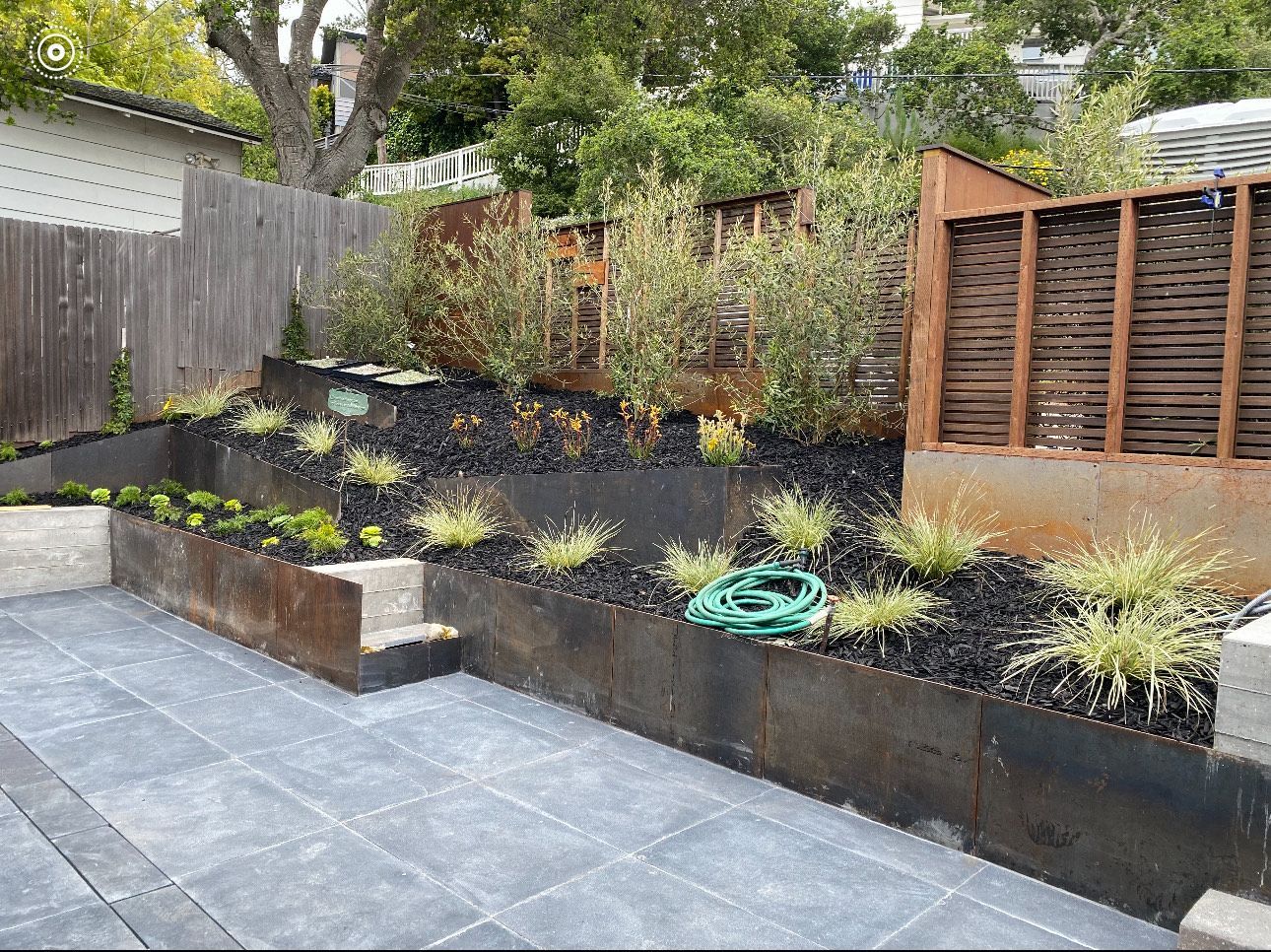 Backyard with tiered garden beds and weathered metal retaining walls.