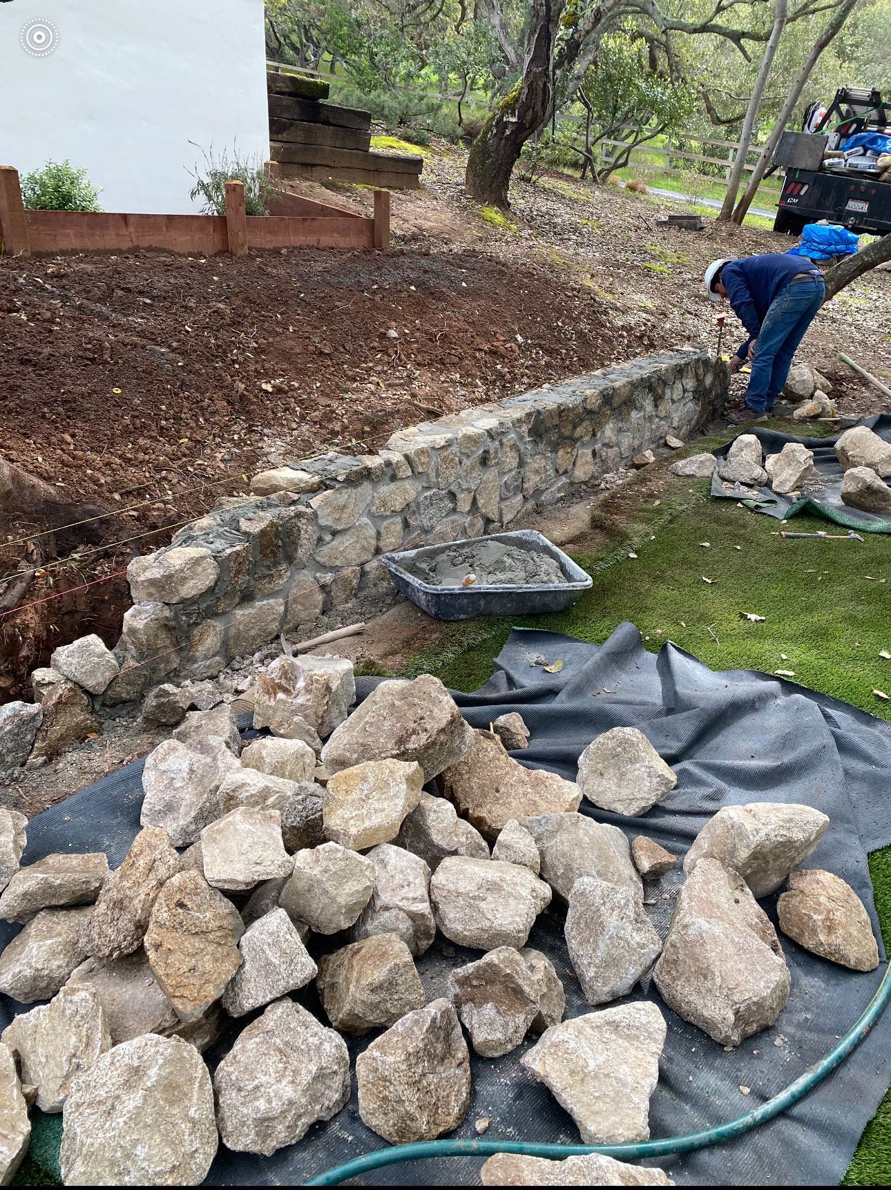 Stone wall construction with a worker placing rocks, a pile of rocks, and a mortar tub.