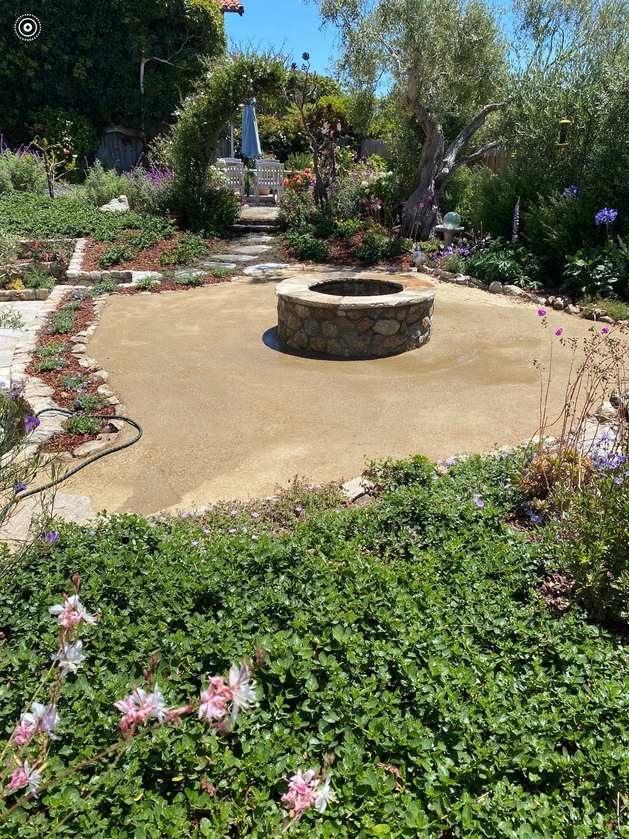 Stone fire pit in a garden surrounded by plants and flowers.