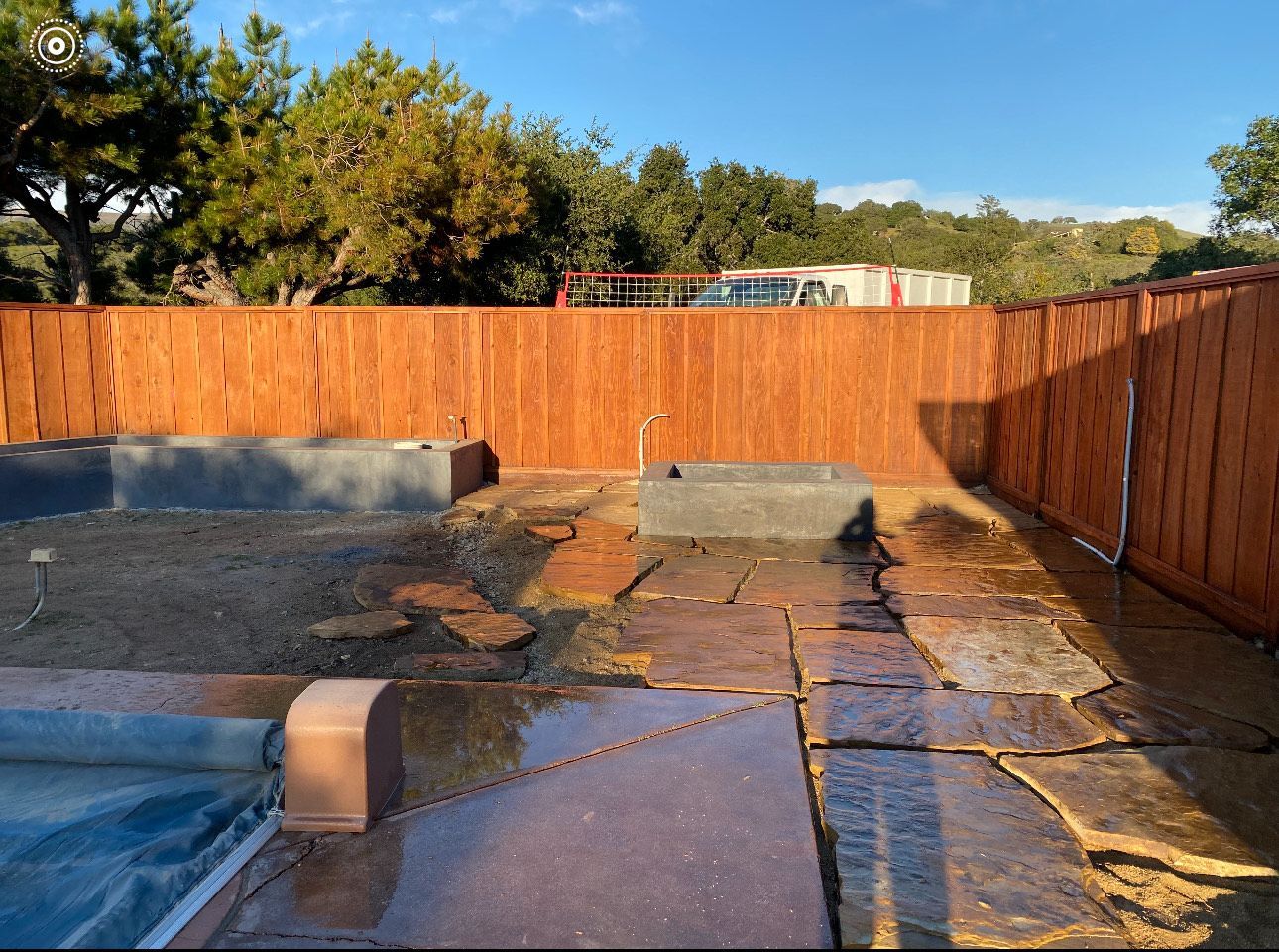 Patio with stone pavers and concrete tubs, surrounded by a stained wooden fence.