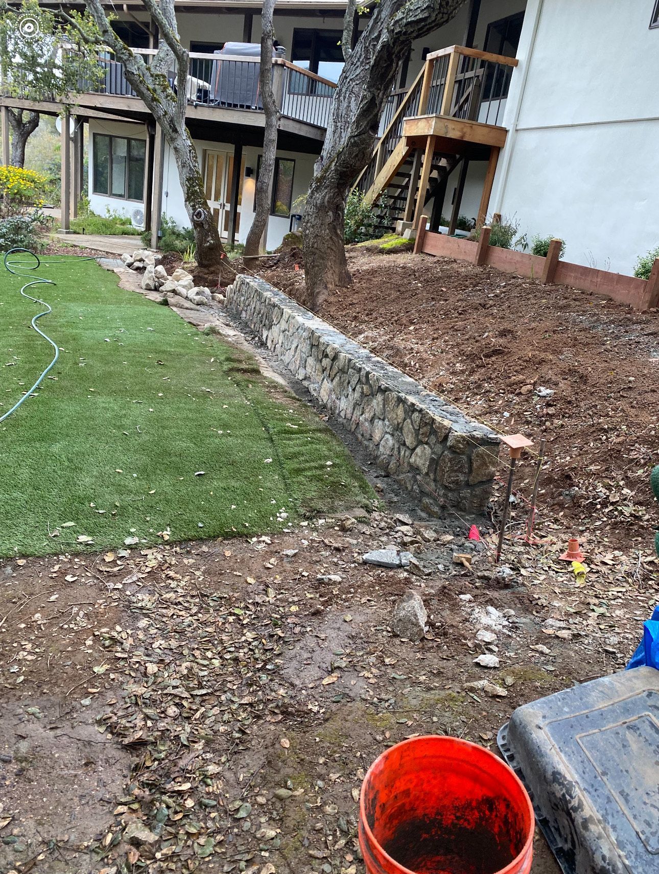 Stone retaining wall next to green turf and a house.