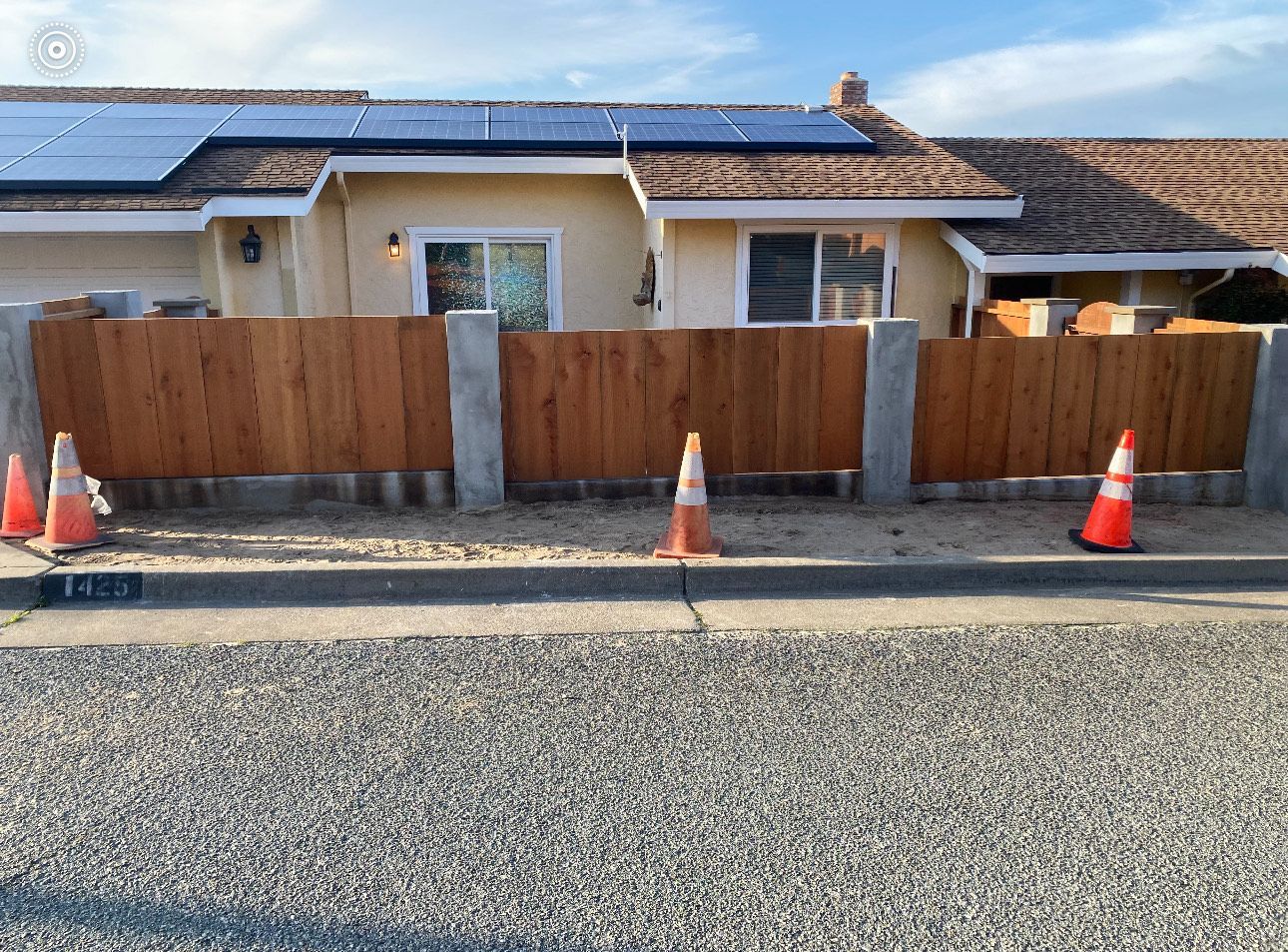 Wooden fence with concrete posts in front of a house, with orange cones on the road.