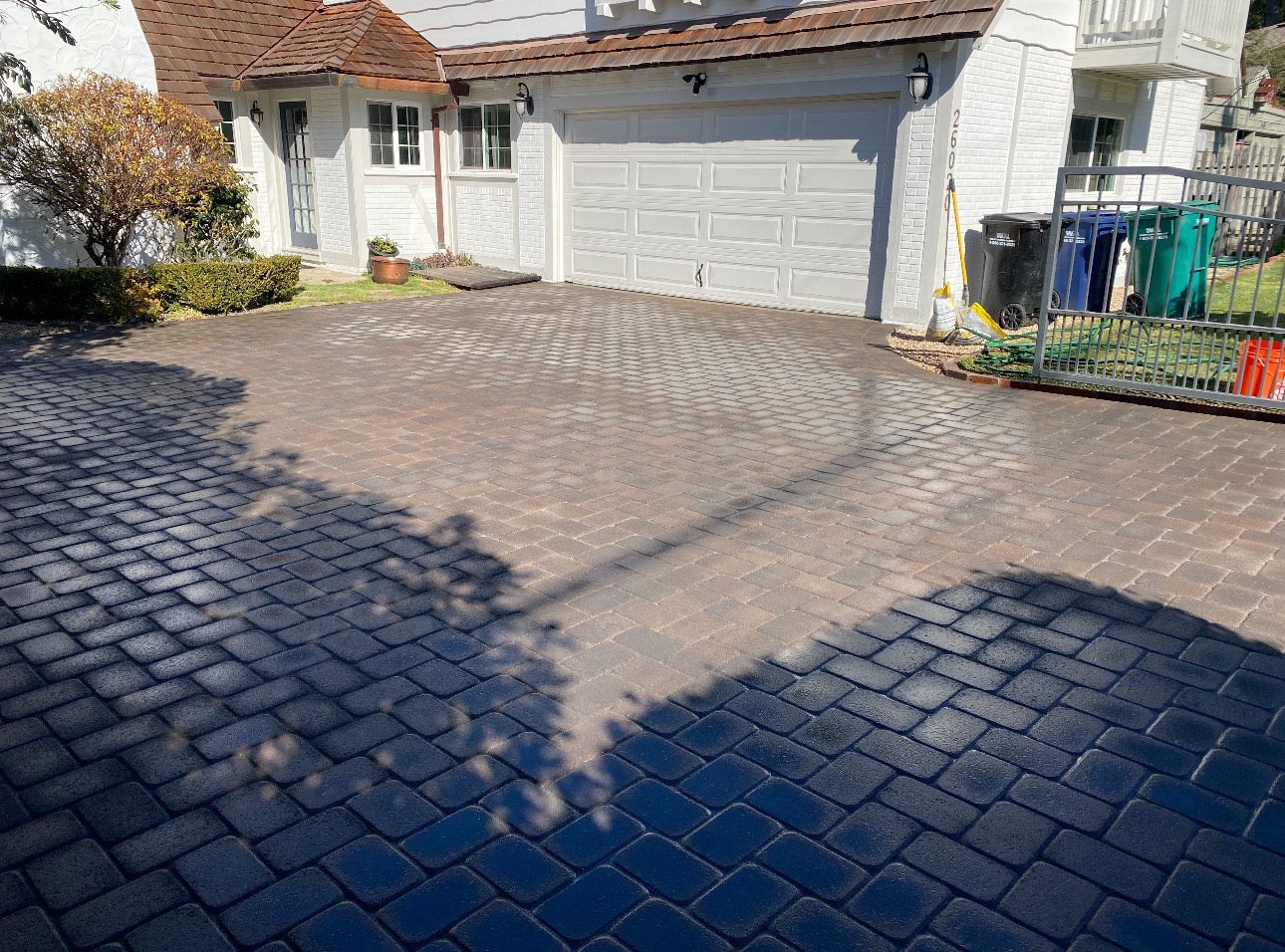 Driveway paved with dark brick leading to a house with a garage. Shadows are cast on the driveway.