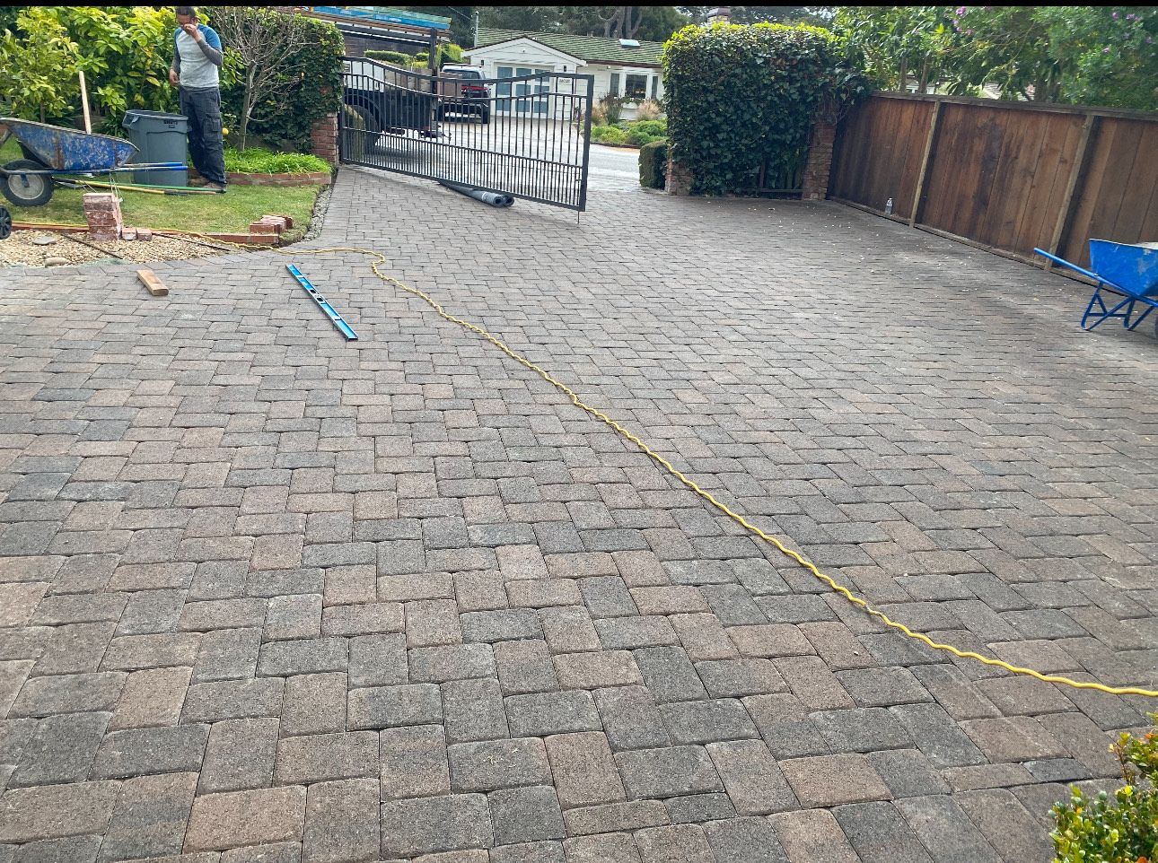 Brick driveway with a yellow measuring tape, person, and gate.