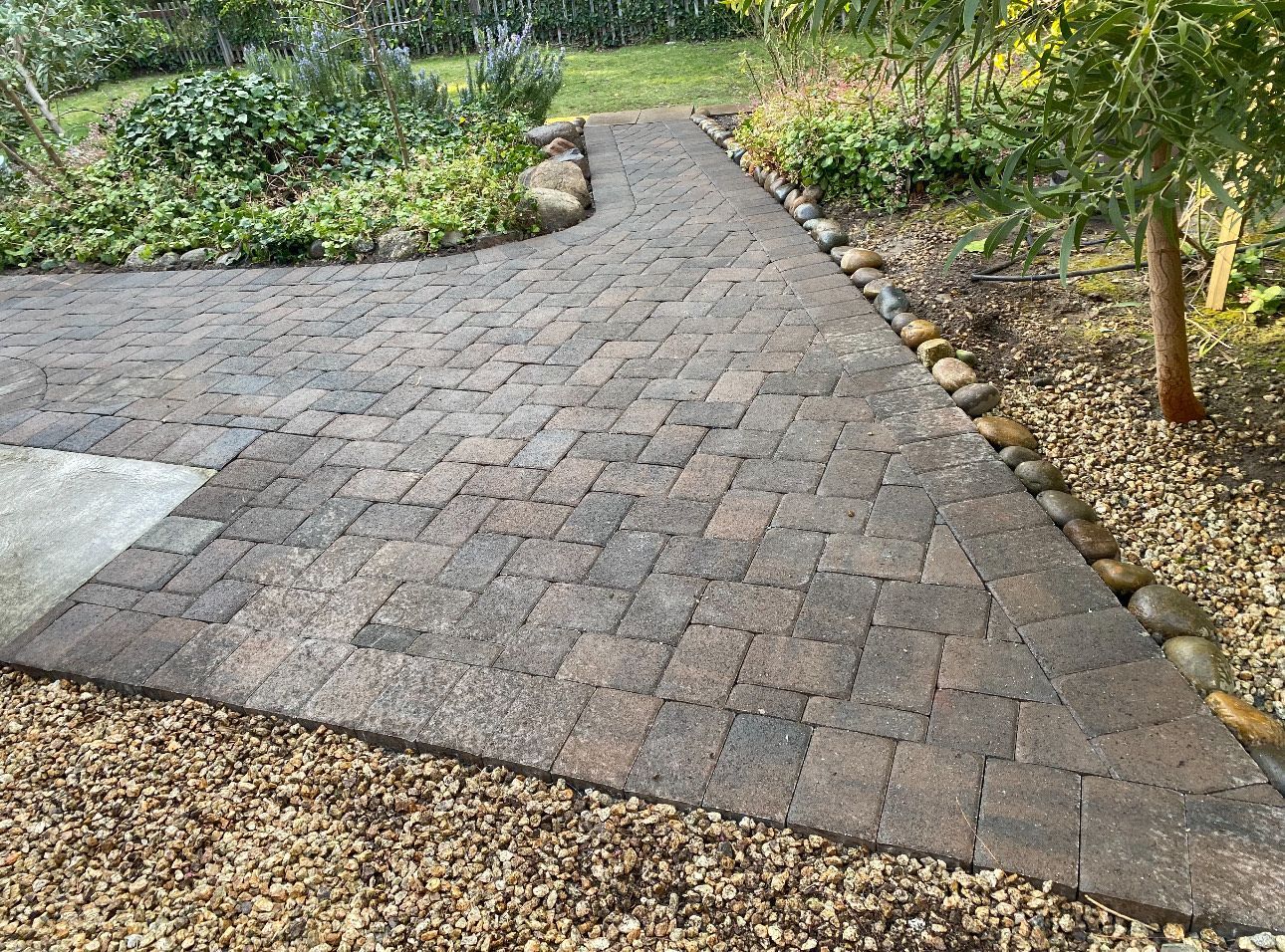 Brick pathway curves through a garden, bordered by gravel and plants.