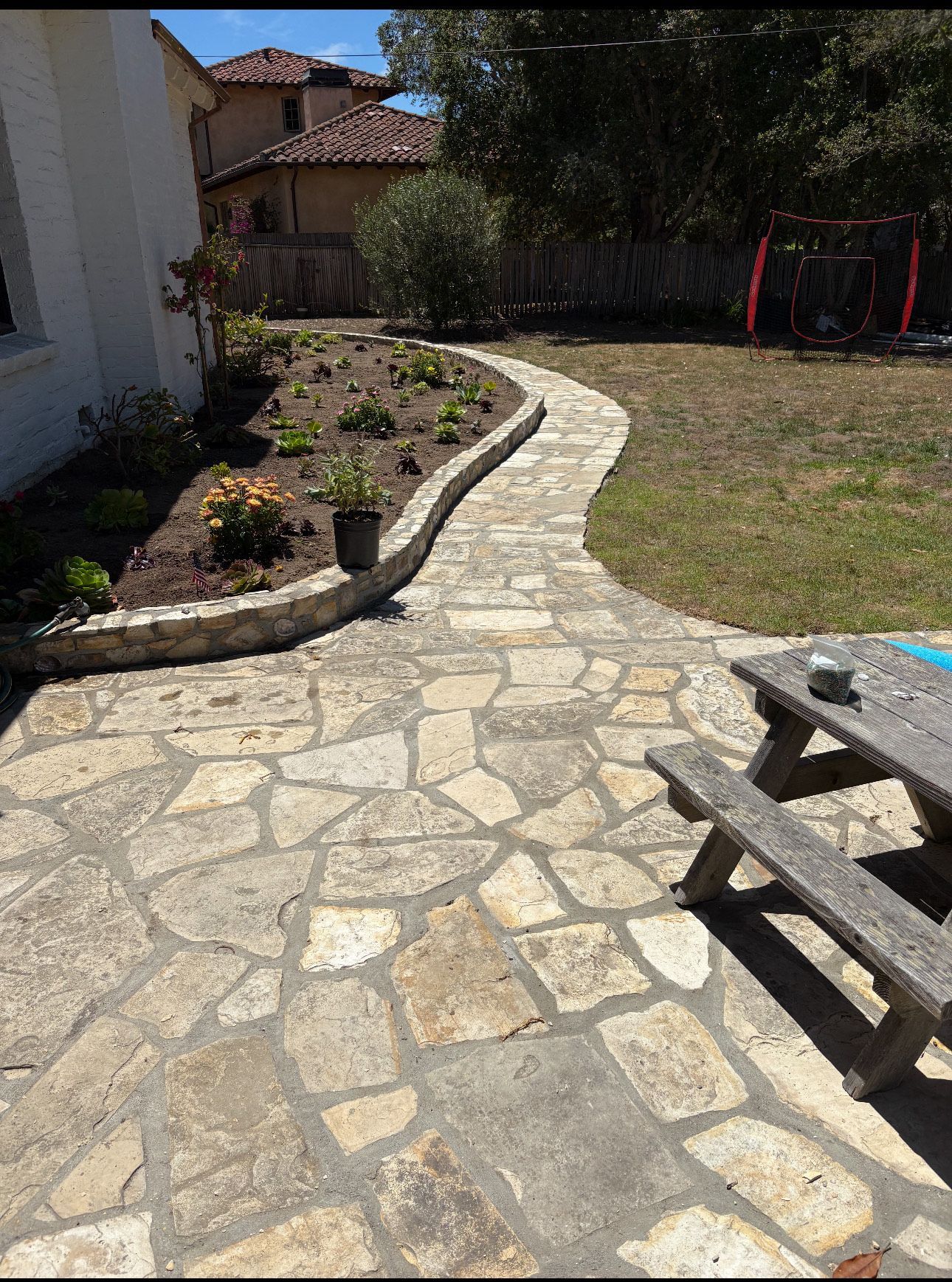 Stone path winds through a yard, past a flower bed, and towards a picnic table.